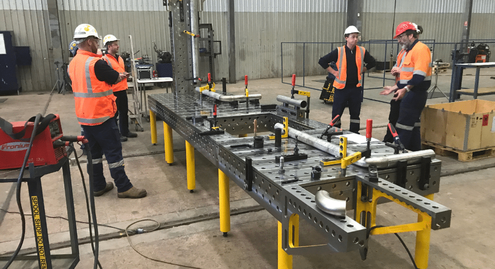 Team of engineers and fabricators discussing a project around a large Demmeler modular welding table in a workshop