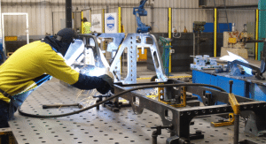 Welder assembling a large metal frame on a Demmeler modular welding table in an industrial workshop