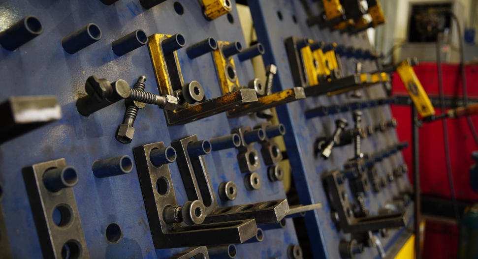 Close-up of a blue Demmeler welding fixture board with organised clamps, stops, and fixturing components mounted in rows