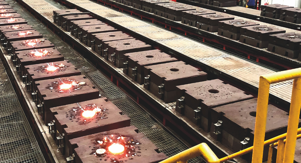 Rows of heavy steel castings or moulds on a foundry production line with glowing molten metal visible in several cavities
