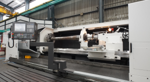 CNC lathe machine with long cylindrical workpiece, featuring control panel on left headstock and tailstock on right, in industrial workshop setting