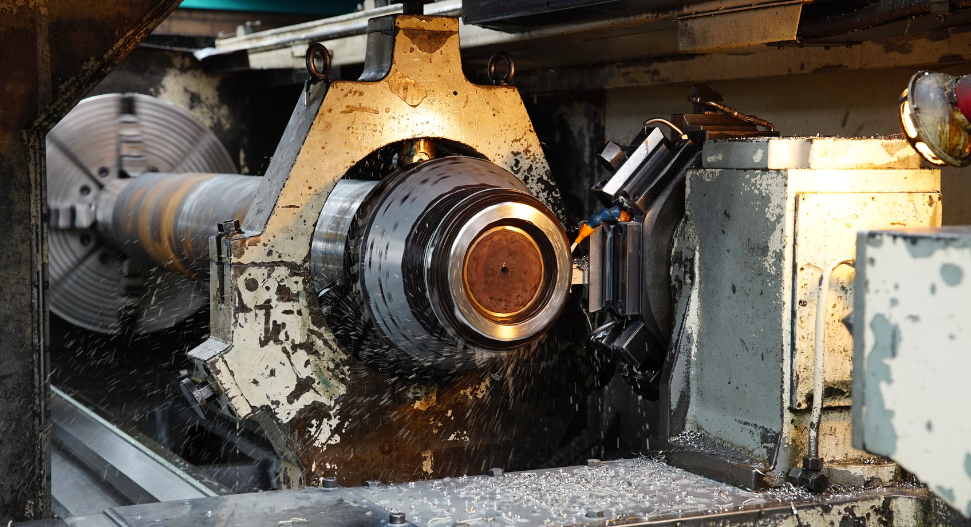 Close-up of a CNC lathe turning a large steel workpiece with coolant spray and metal swarf visible during active machining