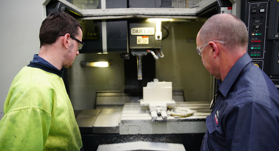 Two CNC machinists inspecting a precision component on a Dahlih vertical machining centre in an Australian engineering workshop