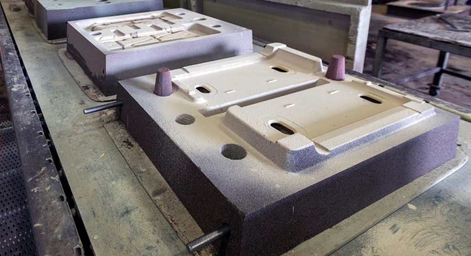 Two sand casting moulds with riser pegs on a foundry workshop bench, ready for metal pouring.