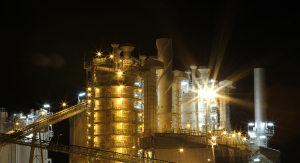 A large industrial plant illuminated at night with bright yellow lights against a dark sky.