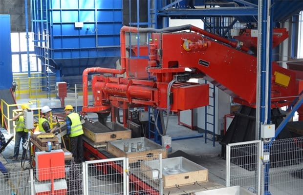 Omega Sinto continuous sand mixer discharging mixed sand into mould boxes on a foundry production line, with integrated dust extraction and automated controls.
