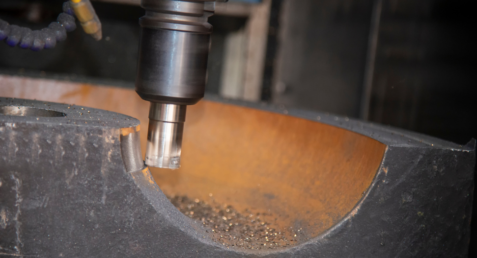 Metal drill bit boring into curved cast steel workpiece with visible swarf and shavings