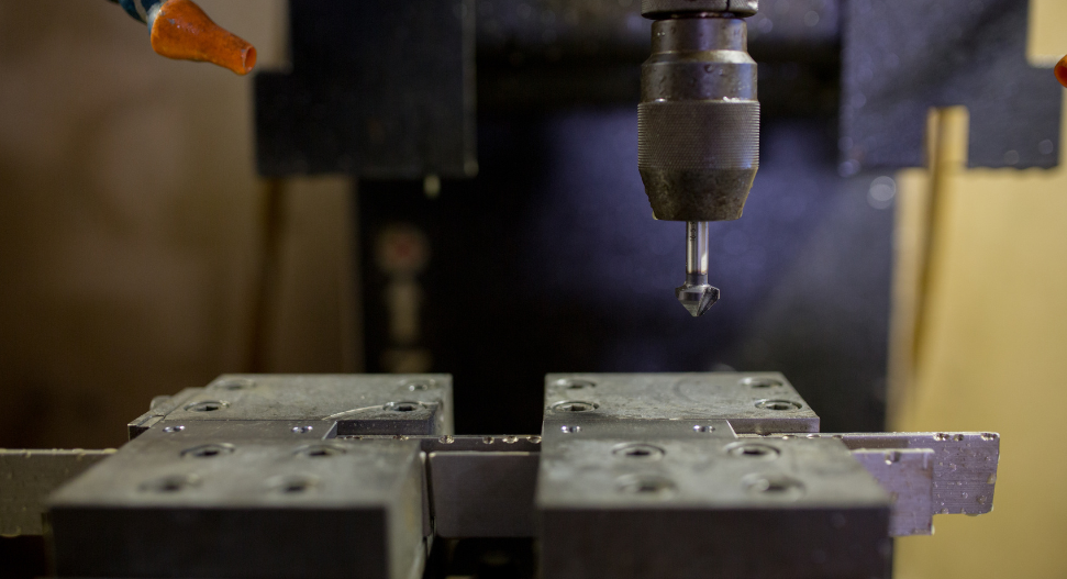 CNC drill press positioned above precision-machined metal mould blocks ready for drilling