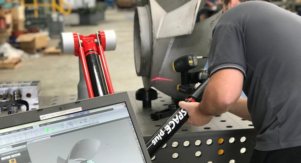 Engineer using handheld 3D scanner to digitise a large metal fan blade component, with CAD model displayed on laptop screen